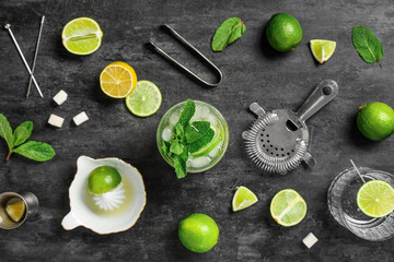 Glass of fresh Mojito cocktail with limes and tools on black background