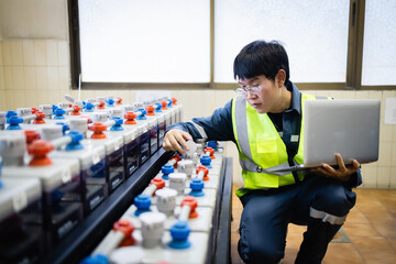 Technician inspects backup power system battery while holding laptop in maintenance room ensuring reliable energy supply and system functionality