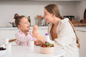 Cute little girl in pajamas with her mom eating yogurt in kitchen