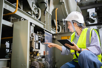 Engineer inspects electric switchgear in gas insulated switchgear GIS field while holding tablet and wearing safety gear to ensure electric grid operates safely and efficiently