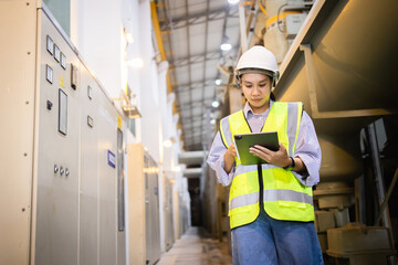 Engineer wearing safety helmet and insulated vest inspects electric switchgear in gas insulated...