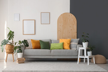 Interior of living room with grey sofa, blank frames and green plants