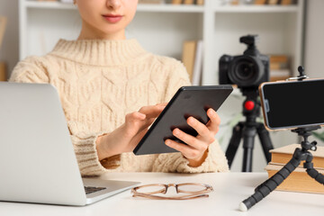 Female blogger using e-reader and laptop on table at home, closeup