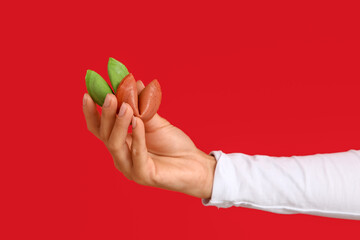 Female hand holding colorful fortune cookies on red background, closeup