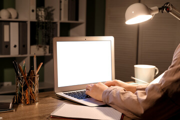 Woman using blank laptop on table in office at night, closeup