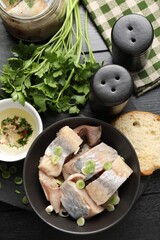 Pieces of delicious herring with green onions on black wooden table, flat lay