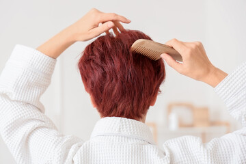 Fototapeta premium Mature woman combing her red hair in bathroom, back view