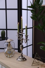 Elegant candlestick with burning candles and decor on table near brown wall