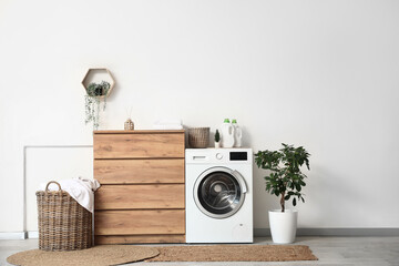 Stylish laundry room with modern washing machine, wooden dresser and bottles of detergent