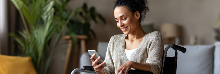 Happy woman in wheelchair is sitting indoors and smiling while using smartphone, enjoying relaxed moment at home