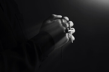 Priest with cross illuminated by holy light praying, closeup. Black-and-white effect