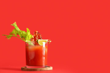 Glass of bloody mary cocktail with bacon, celery and lime on red background