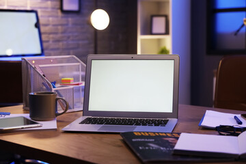 Fototapeta premium Blank laptop with stationery on desk in office at night