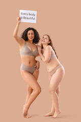Young women in underwear holding paper with text EVERY BODY IS BEAUTIFUL on beige background