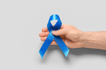 Male hand with blue ribbon on grey background. Prostate cancer awareness concept