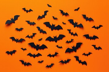 Fototapeta premium Numerous black paper bats arranged on a bright orange background evoking a spooky and festive Halloween atmosphere