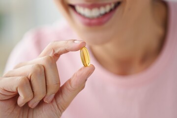 Close-up of a smiling person holding a yellow transparent softgel capsule between fingers, conveying health and positivity