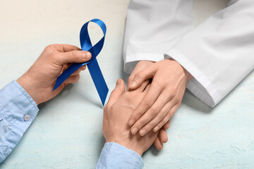 Female doctor supporting man with blue ribbon on light grunge background. Prostate cancer awareness...