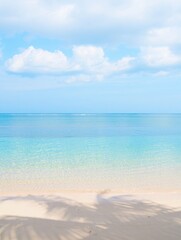 Fototapeta premium Calm beach scene with clear turquoise water, soft sandy shore, light cloud-filled sky, and gentle shadows from nearby palm trees, evoking peace and relaxation
