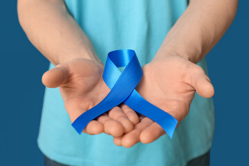 Young man holding blue ribbon on color background. Prostate cancer awareness concept
