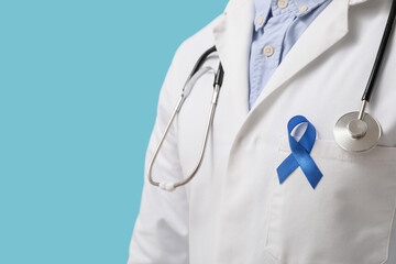 Male doctor with blue ribbon on his uniform against color background. Prostate cancer awareness...
