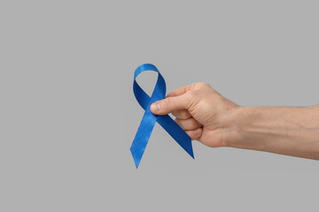 Male hand with blue ribbon on grey background. Prostate cancer awareness concept