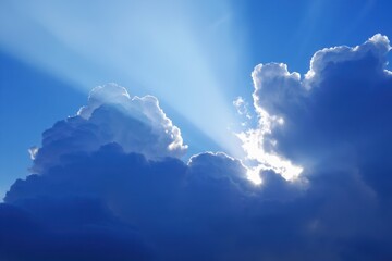 Bright sunlight shining through large fluffy clouds against a clear blue sky creating radiant beams of light