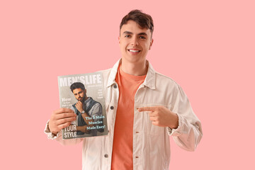 Handsome young man pointing at fashion magazine on pink background