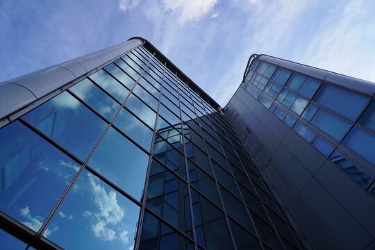 Low angle view of modern glass skyscraper reflecting blue sky and clouds with sleek metallic frame under bright daylight