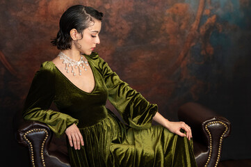 Elegant young woman in vintage green velvet dress posed in luxurious romantic backdrop.