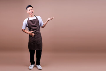 Full Body Of Cheerful Young Barista Male Wearing Brown Apron Presenting Empty Space For Ads Space