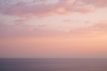 Obraz premium Tranquil ocean under a soft pastel pink and purple sky during sunset with scattered clouds