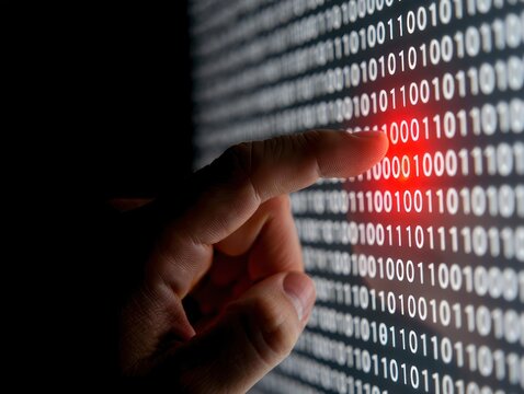Close-up of a human finger touching a brightly lit digital screen displaying rows of binary code with a highlighted red section, symbolizing data interaction and technology