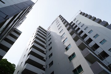 Tall white residential buildings with multiple balconies and windows against a clear sky viewed from below