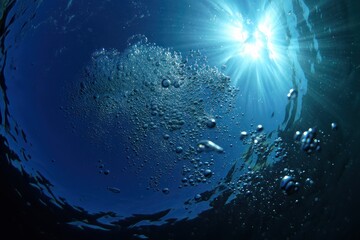 Underwater view of bubbles rising towards the bright sun shining through the deep blue ocean surface
