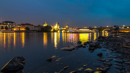 The Charles Bridge day to night timelapse over the Vltava River reflected in water in Prague, Czech...