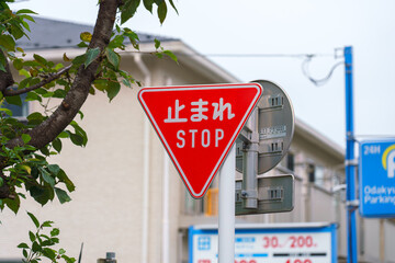 Tokyo, Japan - Sep 30 2024, A close-up view of a triangular red traffic stop sign hanging over the road, with building facades and an cloudy sky in the background, Tokyo, Japan