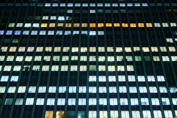 Tokyo, Japan, panoramic view of the facade of an office building at night with lights on in most windows of offices where people work