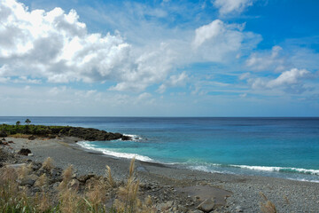 Pebble Beach with Gentle Waves and a Rocky Coastline. A tranquil view of small waves washing onto a pebble beach bordered by rugged rocky formations and coastal greenery.