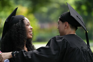 Two graduates in caps and gowns joyfully celebrate, each holding a diploma with smiles and raised...