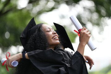 Two graduates in caps and gowns joyfully celebrate, each holding a diploma with smiles and raised...