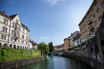 Naklejka premium Scenic view of Ljubljana's riverside architecture featuring classical buildings, stone embankments, and tranquil green waters under bright summer sky in Slovenia's capital