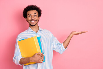 Smiling young man in casual attire holding colorful folders and gesturing against a vibrant pink...