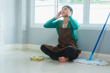 Asian housewife, exhausted after cleaning the room, takes a much-needed break while sitting down,...
