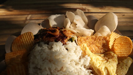Called pecel rice with vegetables and crackers, served on bamboo and sunlight.