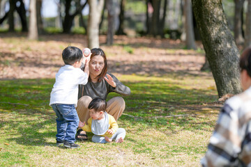 In a sunny forested Japanese park in March, a three-year-old boy throws a baseball toward his father, while his six-month-old sibling sits on the grass with their thirty-something mother beside them.