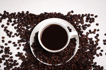 Freshly brewed black coffee in a white cup beside roasted beans on rustic table, capturing morning aroma, warmth, and cozy atmosphere.