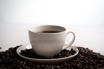 Freshly brewed black coffee in a white cup beside roasted beans on rustic table, capturing morning aroma, warmth, and cozy atmosphere.