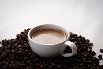 Freshly brewed black coffee in a white cup beside roasted beans on rustic table, capturing morning aroma, warmth, and cozy atmosphere.