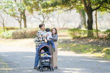 In March, at a sunny forested park in Japan, a Japanese couple walks with their 3-year-old son and...